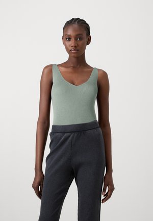 Ribbed green bodysuit with a deep V-neck design, paired with dark grey, textured knit trousers featuring an elastic waistband.