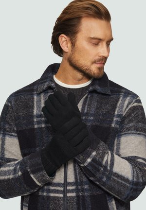 Schwarze, gestrickte Handschuhe mit strukturiertem Grip, getragen von einer Person in einer grauen, blauen und schwarzen karierten Jacke. Die Handschuhe sind eng anliegend.