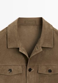 Bruine suède jas met spitse kraag, twee borstzakken met knopen en een knoopsluiting aan de voorkant.