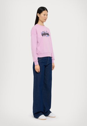 Rosa genser med svart og blå grafikktrykk, kombinert med vide, mørke denimjeans og hvite sko. Enkelt design og avslappet passform.