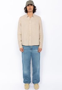 Beige button-up shirt met een gewone weving, lichte denimjeans en beige schoenen. Het shirt heeft een kraag en een relaxte pasvorm.