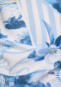 Patterned textile featuring blue and white floral designs, textured fabric with hints of yellow, soft drape, and a mixed graphic style.