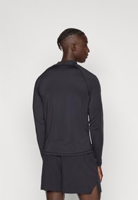 Fekete hosszú ujjú sportfelső kerek nyakkivágással és minimális varrással, hozzáillő rövidnadrággal párosítva. Sima textúra, testhez simuló szabás.