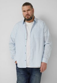 Hellblaues Hemd mit Rautenmuster, durchgeknöpfter Vorderseite und langen Ärmeln, getragen über einem weißen T-Shirt und kombiniert mit dunklen Jeans.