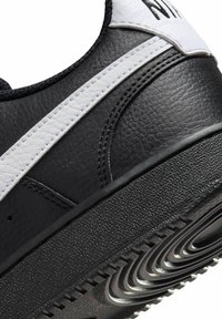 Sneaker in pelle nera con accenti bianchi, superiore testurizzato e suola in gomma con motivi di battistrada ondulati. Dettagli cuciti ai lati.