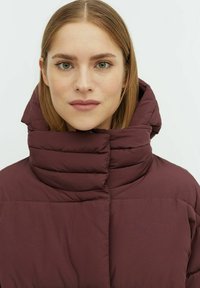 Giacca a vento bordeaux con colletto alto e trapuntato. Presenta cuciture orizzontali e una superficie liscia e lucida. Chiusura con zip completa.