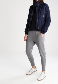 Marineblauer Bomberjacke mit Reißverschluss, graue, schmal zulaufende Sweatpants und weiße Sneakers mit hellblauen Streifen. Sanfte Texturen und lässiges Design.