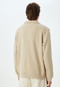 Beige Sweatshirt mit weicher Textur, mit Kragen, gerippten Bündchen und Saum sowie lässiger Passform, mit einem schlichten Rückansicht.