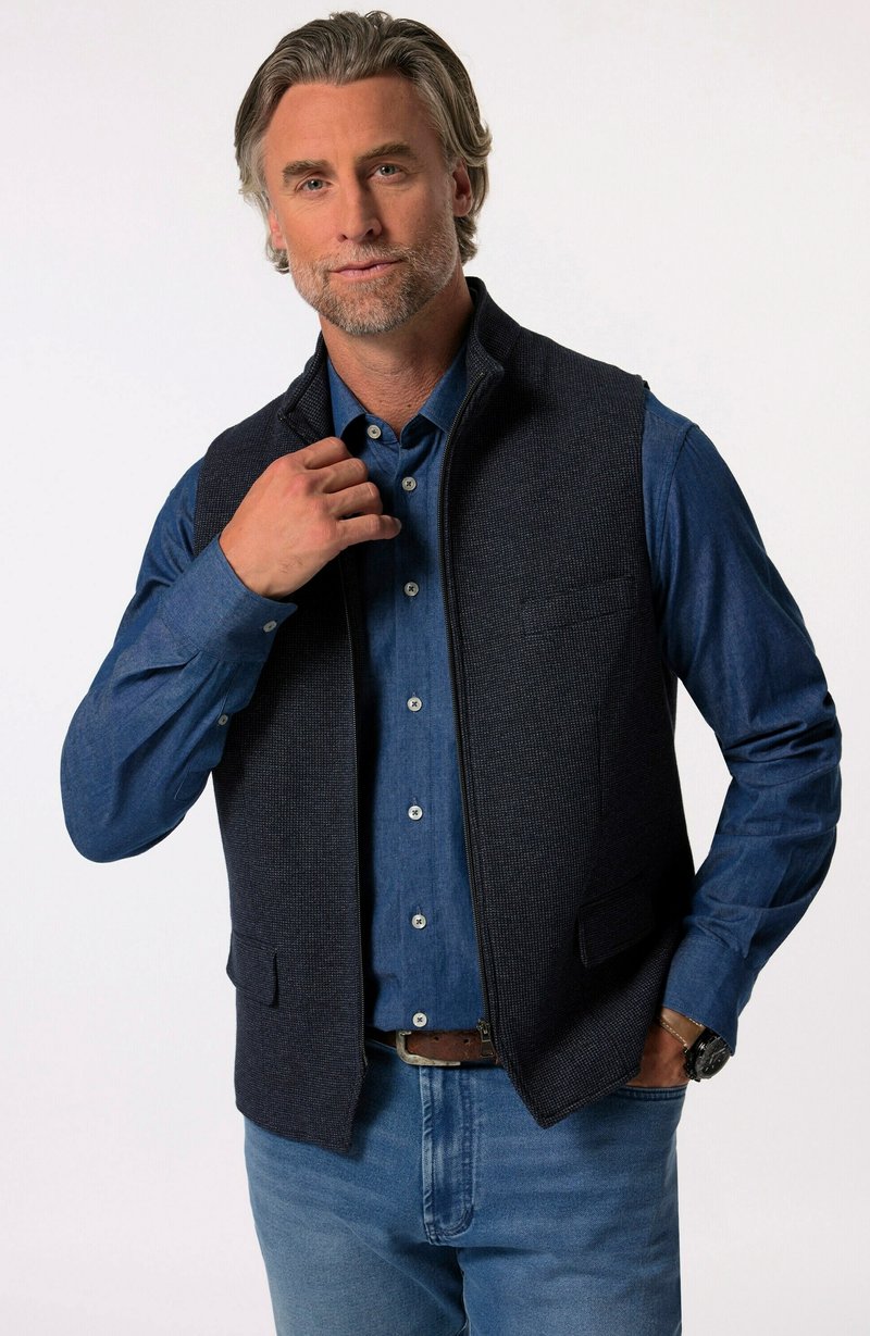 Marineblauer Steppweste mit zwei Fronttaschen, getragen über einem blauen Hemd mit Knöpfen. Verfügt über einen hohen Kragen und einen glatten Reißverschluss.