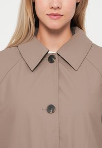 Beige waterproof jacket featuring a pointed collar, two black buttons, and a smooth texture, presented against a neutral background.