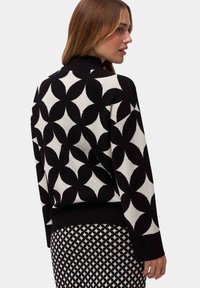 Black and white patterned sweater with a high collar, featuring a floral design. Textured knit and ribbed cuffs and hem.