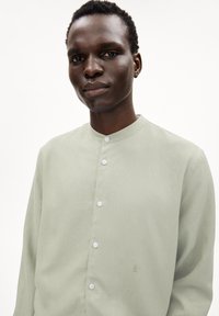 Lichtgroen overhemd met knoopsluiting, voorzien van een mandarin kraag, subtiele structuur en witte knopen; heeft een klein geborduurd detail op de borst.