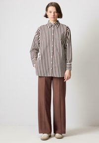 Chemise à rayures marron et crème, avec des manches longues et une poche poitrine, assortie à un pantalon large marron taille haute.