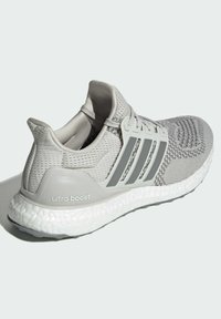 Grå strikket joggesko med teksturert overdel, tre striper som aksent og en hvit Boost-såle. "Ultra Boost"-merking på hælen.