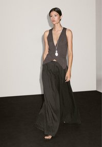 Gray sleeveless top with a V-neck and twist detail, paired with wide black pinstripe pants. Long silver necklace accented. Smooth textures.