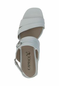 Valkoinen nahkasandaali ristikkäisillä remmeillä, avoimella kärjellä ja nilkkahihnalla. Omintakeinen sileä pinta ja pyöreä korko. "Caprice"-logo sisällä.