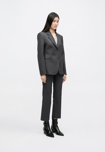 Σκούρο γκρι σακάκι με δύο κουμπιά, συνδυασμένο με παντελόνι στην ίδια απόχρωση και μαύρες μποτάκια μέχρι τον αστράγαλο. Λείος ύφαλος με δομημένο σχέδιο.