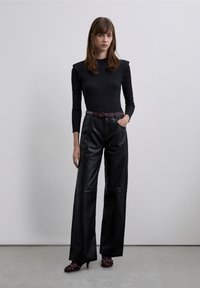 Musta, ribbineuloksinen pitkähihainen paita, räätälöidyt mustat leveälahkeiset nahkahousut, violetti niitillä koristeltu vyö ja avoimet mustat korot, joissa violetit yksityiskohdat.