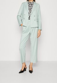 Vaalea mintunvihreä kaksirivinen bleiseri, jossa on siihen sopivat kapenevat housut. Mustat slingback-piikkikorkoiset kengät ja mustavalkoinen seepra-kuviollinen paita.