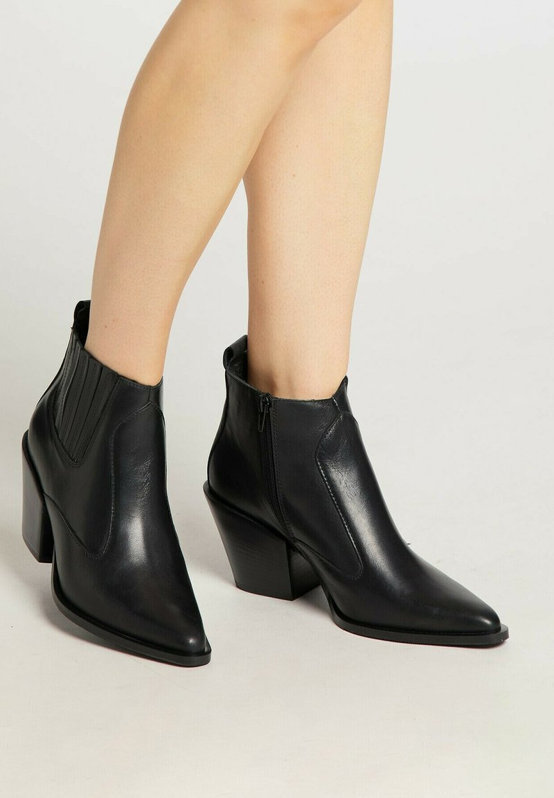 Boots din piele neagră, până la gleznă, cu vârf ascuțit, o pană elastică texturată și un fermoar lateral. Au un toc chunky, înclinat.