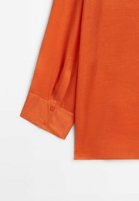 Poignet de chemise à manches longues en tissu orange vif avec deux petits boutons sur le poignet.