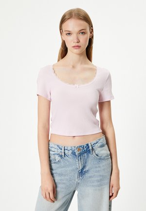 Haut cropped côtelé rose clair avec des manches courtes, présentant un col en dentelle à bordure festonnée et un petit nœud au centre.