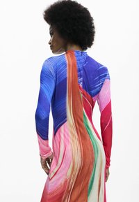 Hosszú ujjú, többszínű ruha, amely kék, rózsaszín, piros és zöld áramló mintával rendelkezik. Simább, rugalmas anyagból készült.
