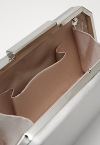 Interiér stříbrné kovové kabelky s klipem s hladkým, světle béžovým textilním podšívkou, obsahující dvě přihrádky a jemnou pruhovanou texturu.