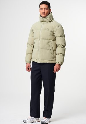 Hellgrüne gepolsterte Jacke mit hohem Kragen, Frontreißverschluss und Seitentaschen, kombiniert mit marineblauen Hosen und grauen Laufschuhen.