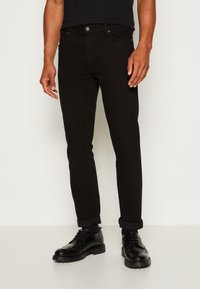 Svarta slim-fit jeans med en slät textur, med knäppning, sidofickor och uppvikta fållar, tillsammans med svarta snörskor.