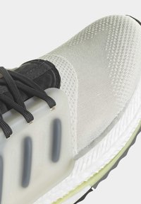 Sko med en sort mesh-overdel og en struktureret hvid panel, gennemsigtig sål og sorte snørebånd, kombineret med en polstret hvid mellemsål.