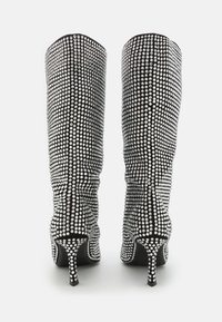 Botas negras hasta la rodilla cubiertas de rhinestones transparentes, con un delgado tacón de aguja y un diseño de tela texturizada. Detalle de fruncido visible.