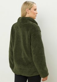 Olijfgroene fleece jacket met een zachte, gestructureerde afwerking, voorzien van een hoge kraag en een losse pasvorm, die tot halverwege de heup reikt.