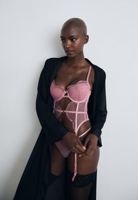 Pink lace lingerie with embroidery features a structured bodice, adjustable straps, and a sheer panel. A black robe drapes over the outfit.
