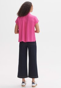 Blusa a maniche corte di un brillante colore rosa, con una piega sul retro, abbinata a jeans in denim scuro a gamba larga e sneakers bianche con dettagli blu navy.