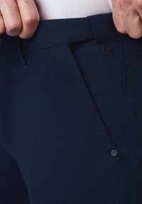 Granatowe spodnie wykonane z teksturowanej tkaniny, z zapięciem na guzik i skośnymi kieszeniami, z delikatnymi szwami wzdłuż pasa.