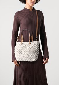 Woven white bag with brown leather handles and strap, featuring a textured design. Structured shape and medium size, suitable for daily use.