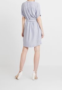 Pasiasta sukienka z krótkimi rękawami, wcięciem w talii i zwiewną sylwetką, wykonana z lekkiego materiału w niebiesko-białe paski. Białe sandały na obcasach.