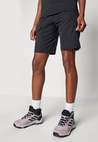 Czarne szorty cargo o luźnym kroju, z bocznymi kieszeniami. Noszone z jasnoróżowymi butami do hikingów i białymi skarpetkami do kostek.