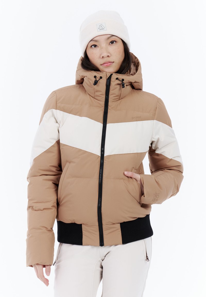 Hnedá puffa bunda s bielym šípkovým pruhom, nastaviteľnou kapucňou a čiernymi rebrovanými manžetami, doplnená svetlou čiapkou.