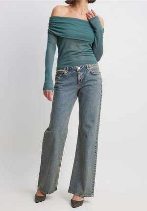 Top teal scollato con dettagli arricciati, abbinato a jeans a gamba larga blu chiaro e scarpe con tacco grigie. Tessuto morbido, design casual.