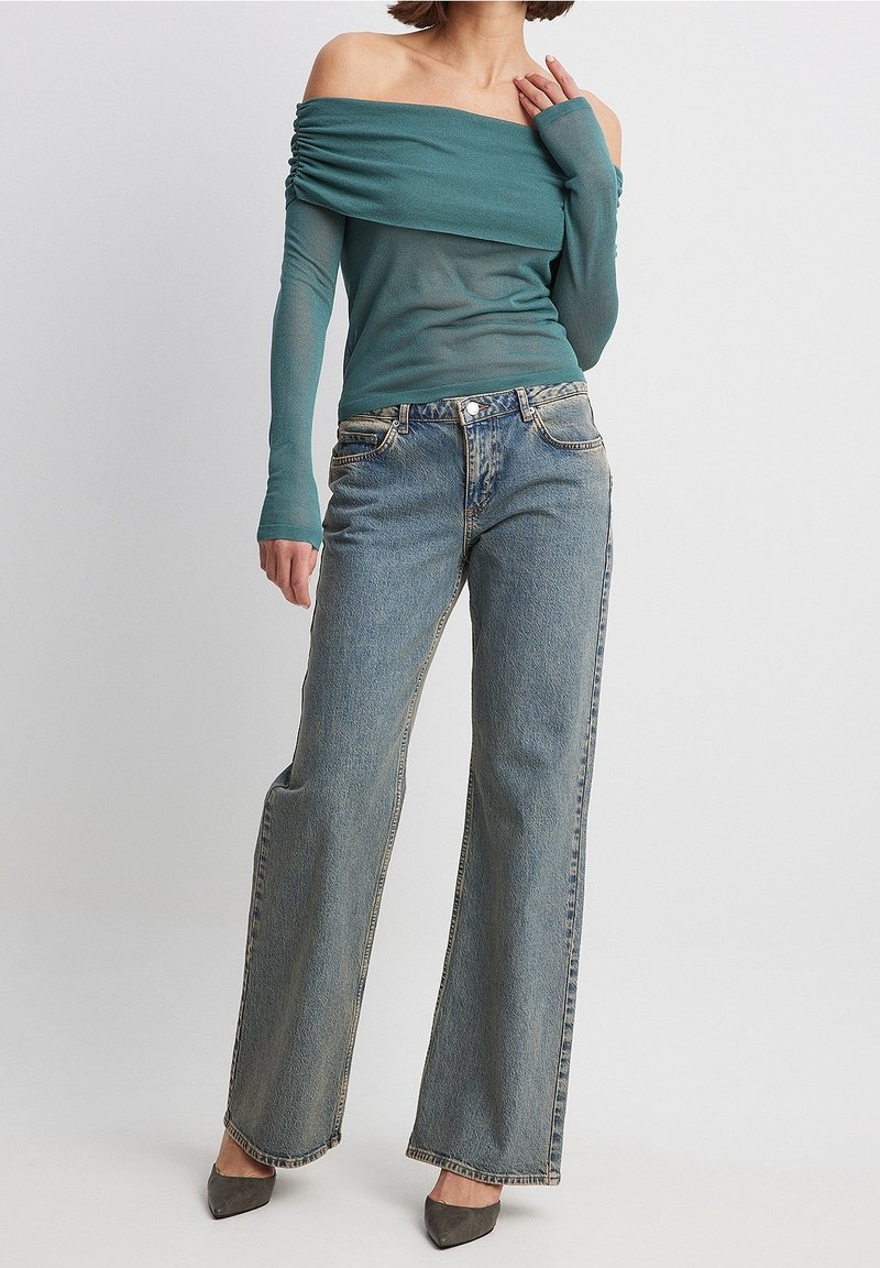 Türkisfarbenes schulterfreies Oberteil mit Raffung, kombiniert mit hellblauen weit geschnittenen Jeans und grauen Absatzschuhen. Glatte Textur, lässiges Design.