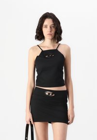 Svart avkortet tanktop og miniskjørt, begge med utskjæringer og tynne stropper. Laget av glatt stoff med en tettsittende design.