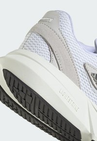 Zapatilla deportiva blanca con materiales de malla y ante, que presenta una gruesa entresuela blanca y una suela negra con agarre texturizado. Logotipo de Lightstrike visible.