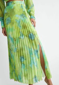 Gonna maxi plissè in tessuto trasparente e leggero. Base verde con acquerelli blu e gialli. Spacco alto a destra per un movimento maggiore.