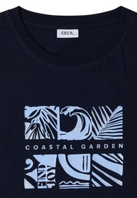 Camisa azul marino con gráfico blanco de elementos costeros abstractos que incluyen hojas de palma, olas y texto "COASTAL GARDEN" y "ENJOY."