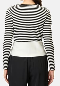 Czarny i biały sweter w paski z długim rękawem, z dopasowaną białą dolną częścią, z teksturą prążkowaną i okrągłym dekoltem.