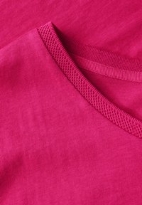 Fuchsiová bavlněná tkanina s hladkou texturou, se žebrovaným výstřihem a mírně zakřiveným tvarem.