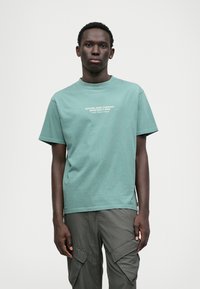 Tricou verde menta cu mânecă scurtă, guler rotund, cu text alb "RIPCURL SURF COMPANY SINCE SIXTY NINE." Fabrică de bumbac neted.