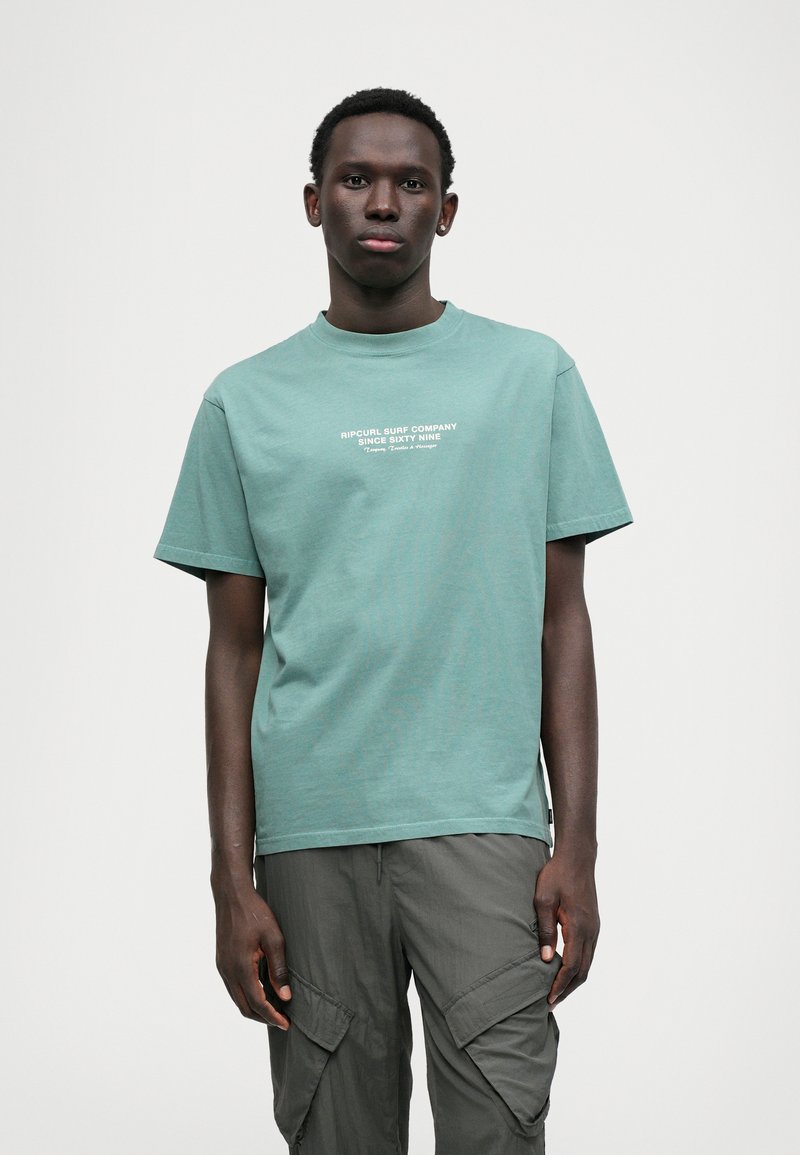 Tricou verde menta cu mânecă scurtă, guler rotund, cu text alb "RIPCURL SURF COMPANY SINCE SIXTY NINE." Fabrică de bumbac neted.